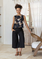 Woman poses in sleeveless, relaxed fit boxy top with high round neckline, and side bust darts in floral print on a black base.