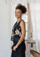 Model stands sideways wearing a sleeveless floral cotton boxy top paired with black cotton pants.