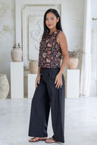 Model stands slightly sideways wearing a sleeveless floral cotton boxy top paired with black cotton pants.