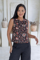 Model poses in sleeveless cotton top in black based floral print with high round neckline and side bust darts.