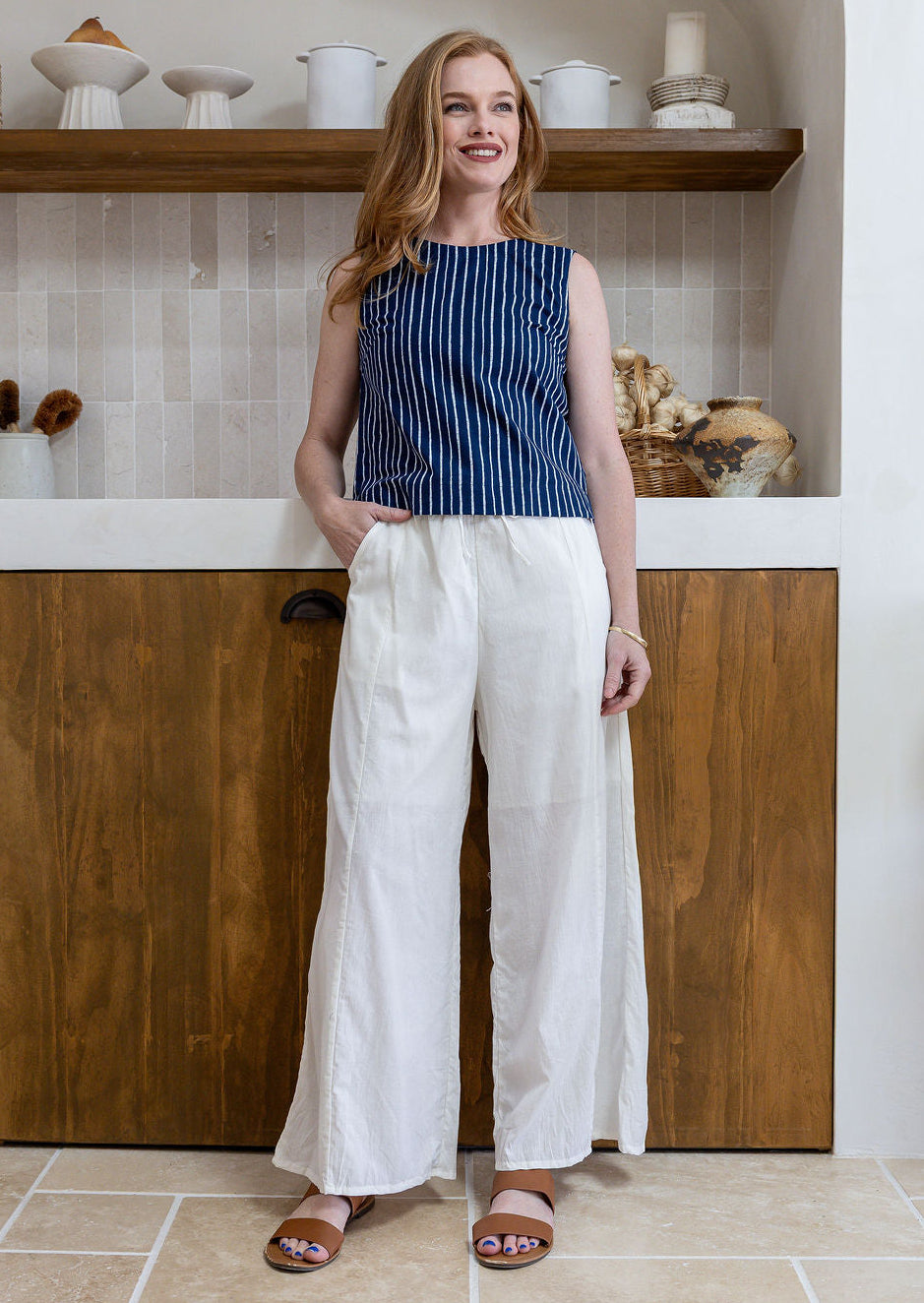 Model stands in white plain pants and relaxed fit floral print top with round neckline, sleeveless design and side bust darts.