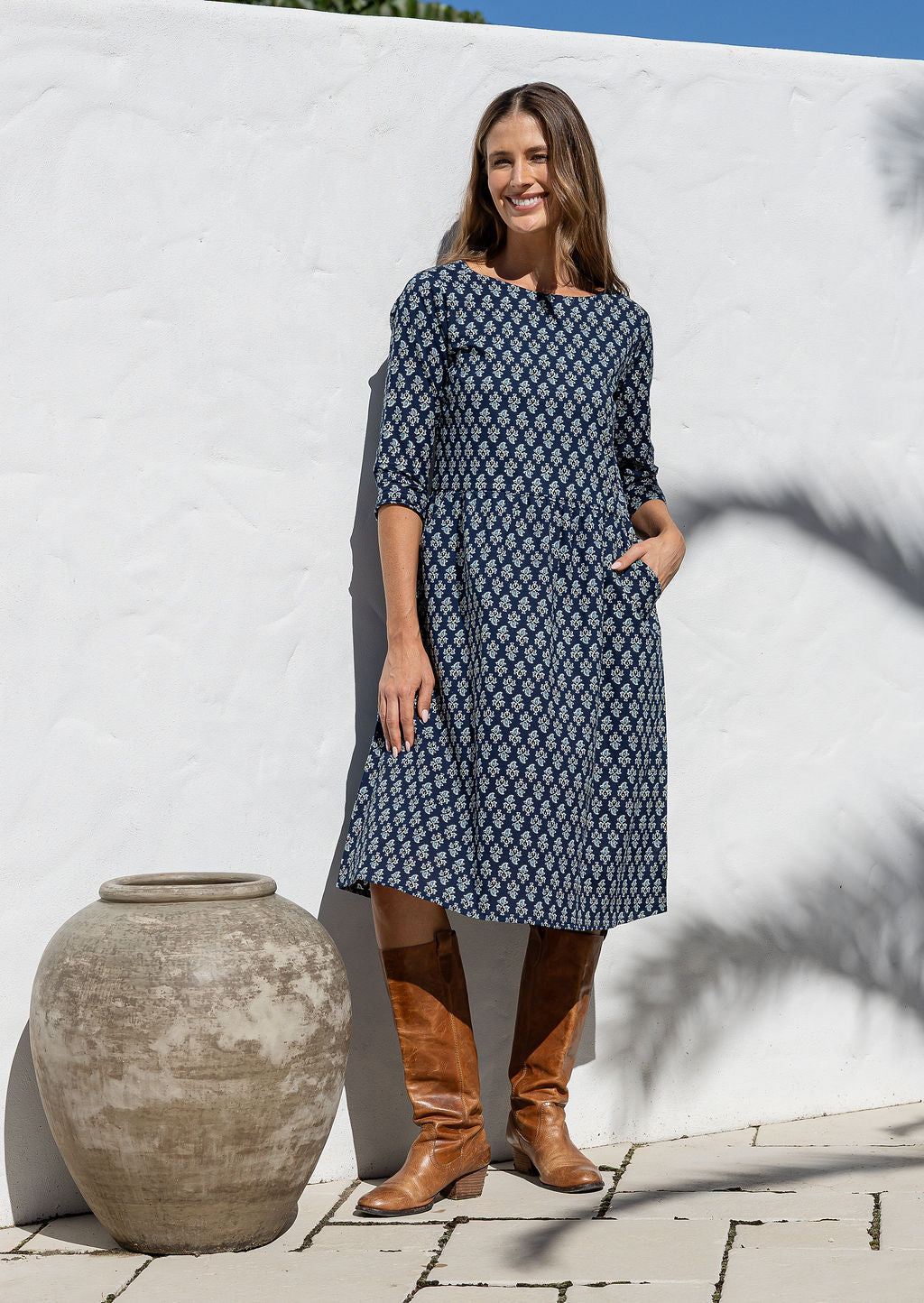 Model poses in navy blue based knee length cotton dress with 3/4 sleeves, round neckline. 