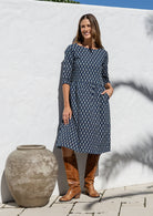 Model poses in navy blue based knee length cotton dress with 3/4 sleeves, round neckline. 