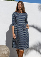Model wears navy blue based knee length cotton dress with 3/4 sleeves, round neckline and one hand in pocket.