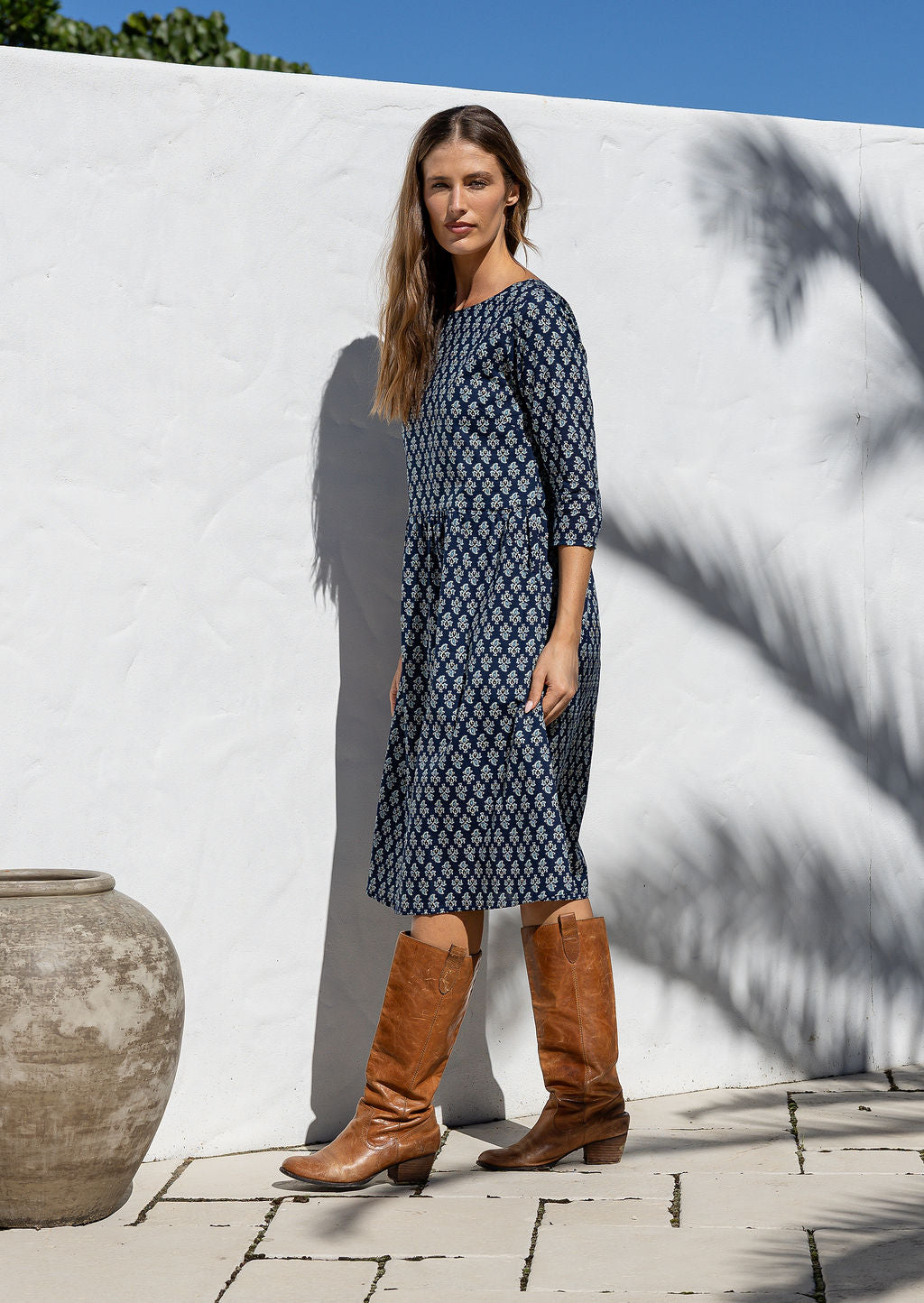 Model standing sideways wearing a relaxed fit cotton dress sitting just below the knee length with wide round neckline.
