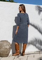Model standing backwards wearing a relaxed fit cotton dress sitting just below the knee length in navy blue based floral print.