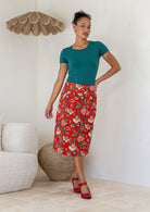 Woman wearing a high-waisted, knee length pencil skirt with piped detailing and pockets in a red based floral print.