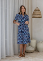 Woman standing in printed shirt dress with detachable fabric belt, short sleeves and pockets.