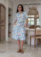 Model poses wearing a shirt style button through cotton dress with collar and a removable waist tie.