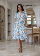 Model poses wearing a shirt style button through cotton dress with collar and a removable waist tie.
