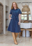 Woman wearing 100 percent cotton button through shirt dress with collar and short sleeves, in a navy based white striped print. 