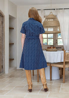 Model stands backwards wears 1950s inspired, button through shirt style dress with collar, short sleeves, waist tie and pockets.