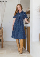 Model poses wearing a shirt style button through cotton dress with collar and a removable waist tie.