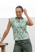 woman standing wearing a sage green based floral printed slim fit shirt against a white background. 