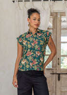 Woman wearing a green based floral printed slim fit shirt in a home setting.