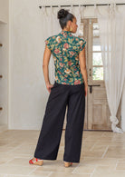 woman standing backwards wearing a green based floral printed slim fit shirt, in a room setting.