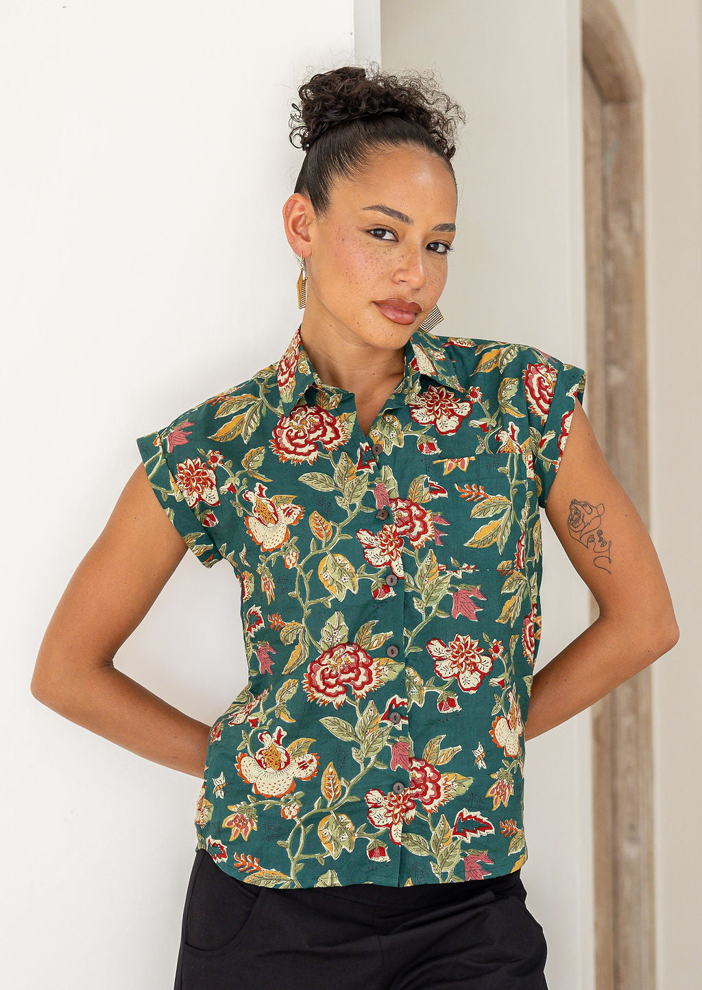 Woman wearing a 100% cotton green based floral top against a white wall
