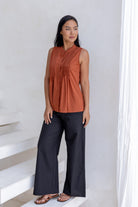 Woman wearing a fitted sleeveless cotton top in rust shade with small pin tuck detailing at the front and back. 