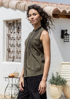 Woman stands sideways wearing 100% cotton, sleeveless top with buttoned mandarin collar, round neckline and decorative small pleated design in front.