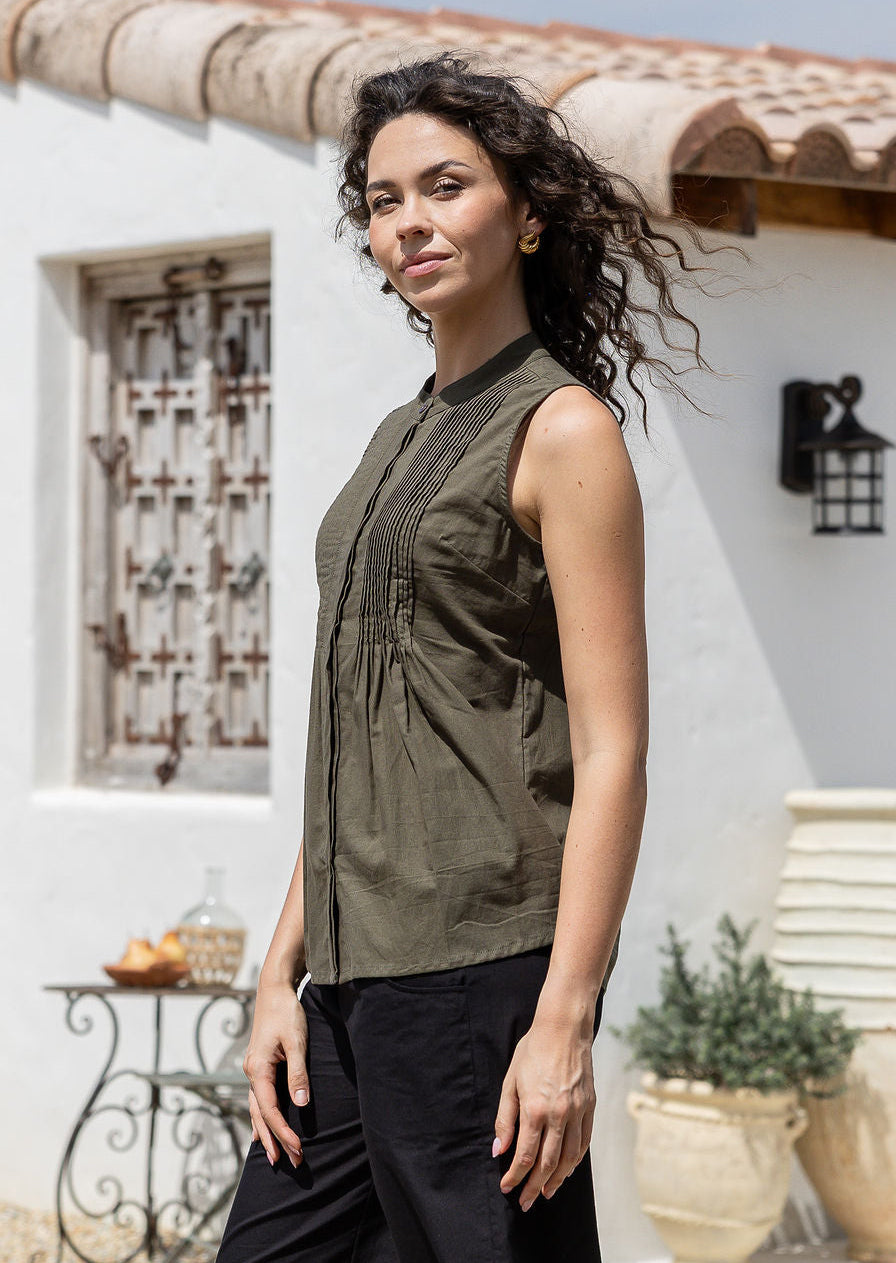 Woman stands sideways wearing 100% cotton, sleeveless top with buttoned mandarin collar, round neckline and decorative small pleated design in front.