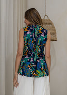Woman stands backwards wearing a navy based floral print sleeveless cotton top with buttoned mandarin collar, high round neckline and flared fit