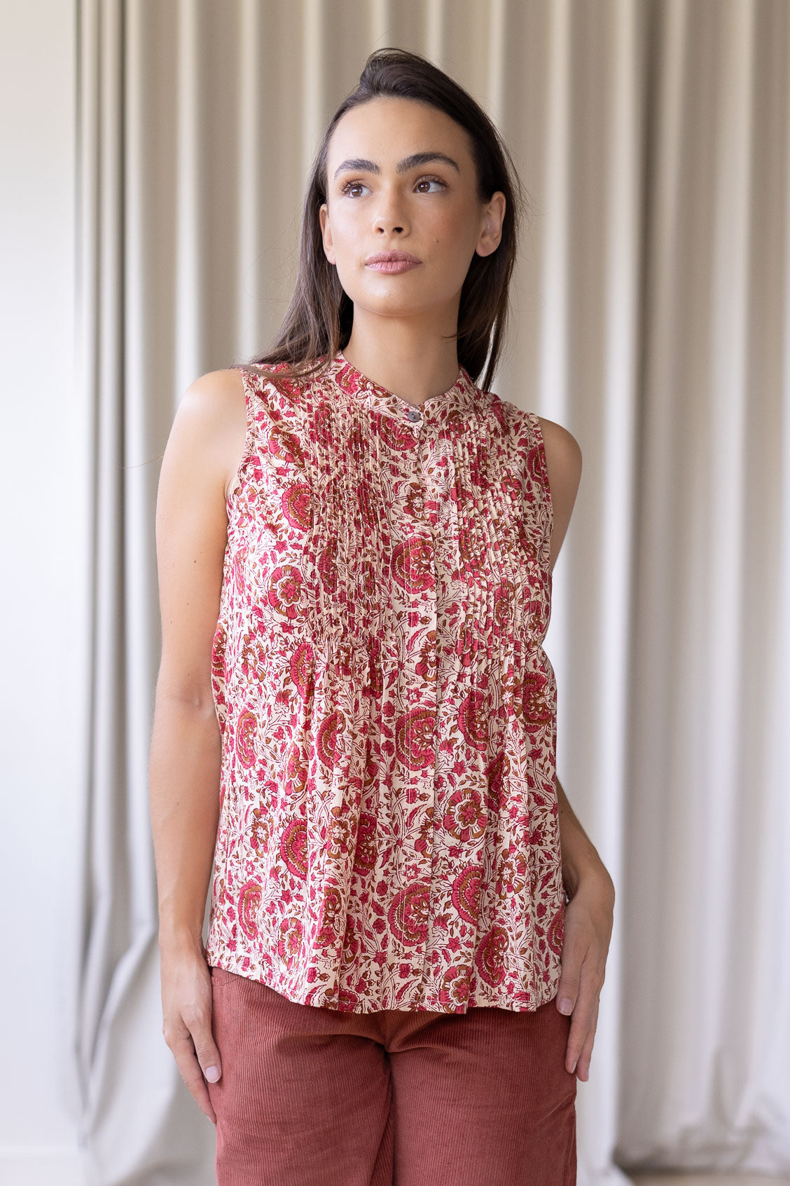 Woman posing in a minimalistic room wearing a cotton sleeveless top in gentle cream based floral print with small decorative pleats in the front.