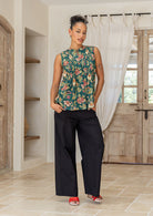 Woman posing in a minimalistic room wearing a cotton sleeveless top in green based floral print with small decorative pleats in the front.