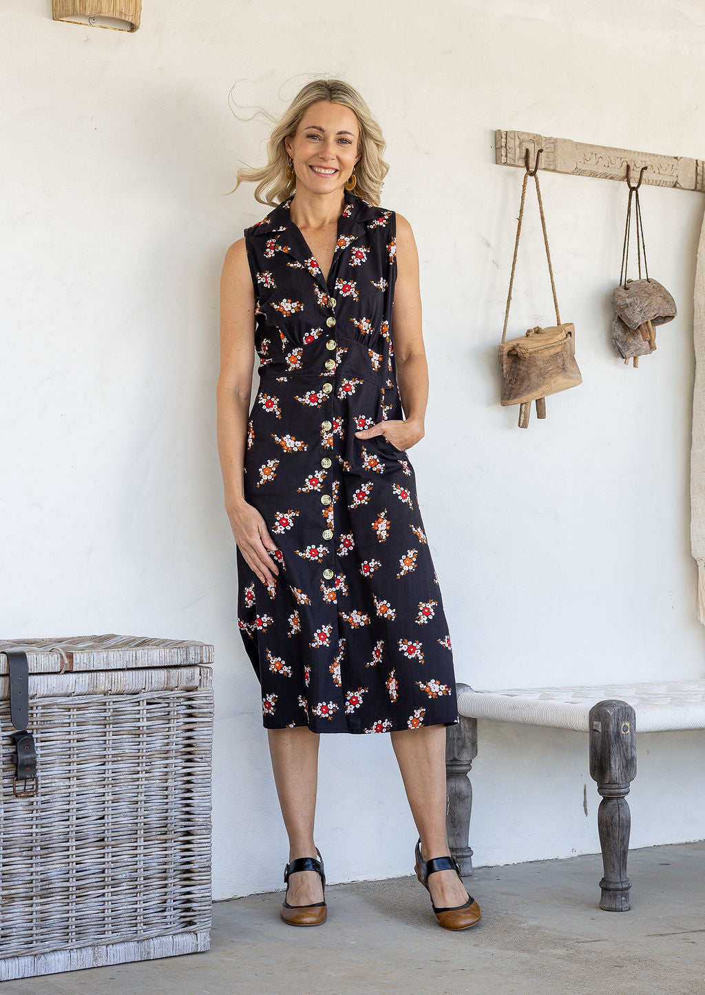 Woman wearing midi length, sleeveless  cotton dress with collar and pockets in black based floral print.