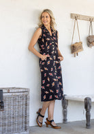 Woman wearing midi length, sleeveless  cotton dress with collar and pockets in black based floral print.