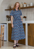 Woman wearing 100 percent cotton button through shirt dress with collar and short sleeves, in a navy based floral print. 