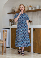 Model poses wearing a shirt style button through cotton dress with collar and a removable waist tie.