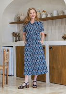 Model standing with both hand in pockets wearing a floral printed shirt dress with detachable fabric belt and short sleeves 