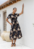 Woman in a floral dress standing against a white wall with decorative elements.