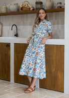Woman wearing 100 percent cotton button through shirt dress with collar and short sleeves, in a white based floral print. 
