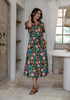 Model standing with one hand in pocket wearing a floral printed shirt dress with detachable fabric belt and short sleeves 