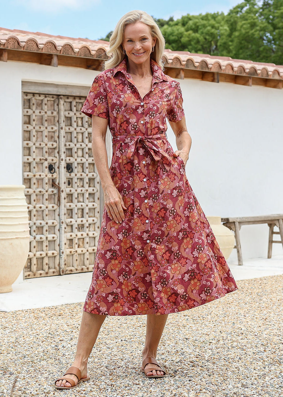 Woman wears 100% cotton warm toned button through shirt style dress with pockets, collar, short sleeves and a fabric waist tie.