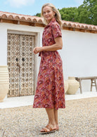 Woman standing in a midi length 1950s style shirt dress with structured collar, short sleeves, waist tie and pockets. 