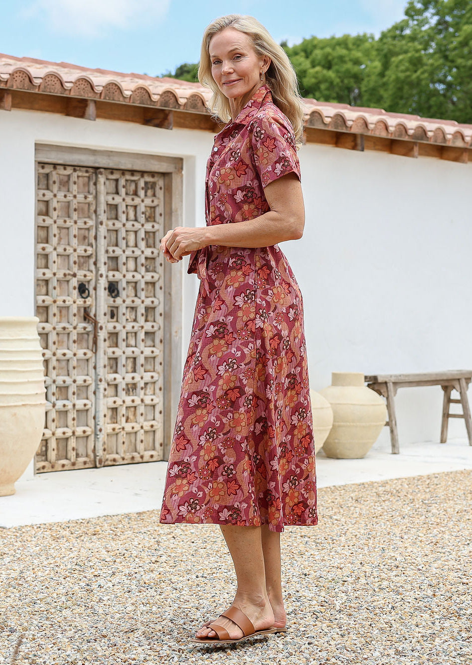 Woman standing in a midi length 1950s style shirt dress with structured collar, short sleeves, waist tie and pockets. 