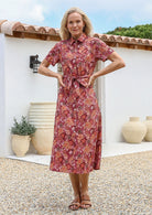 Woman standing outdoors wears 100% cotton warm toned midi length dress with shirt sleeves, collar and removable fabric waist tie.