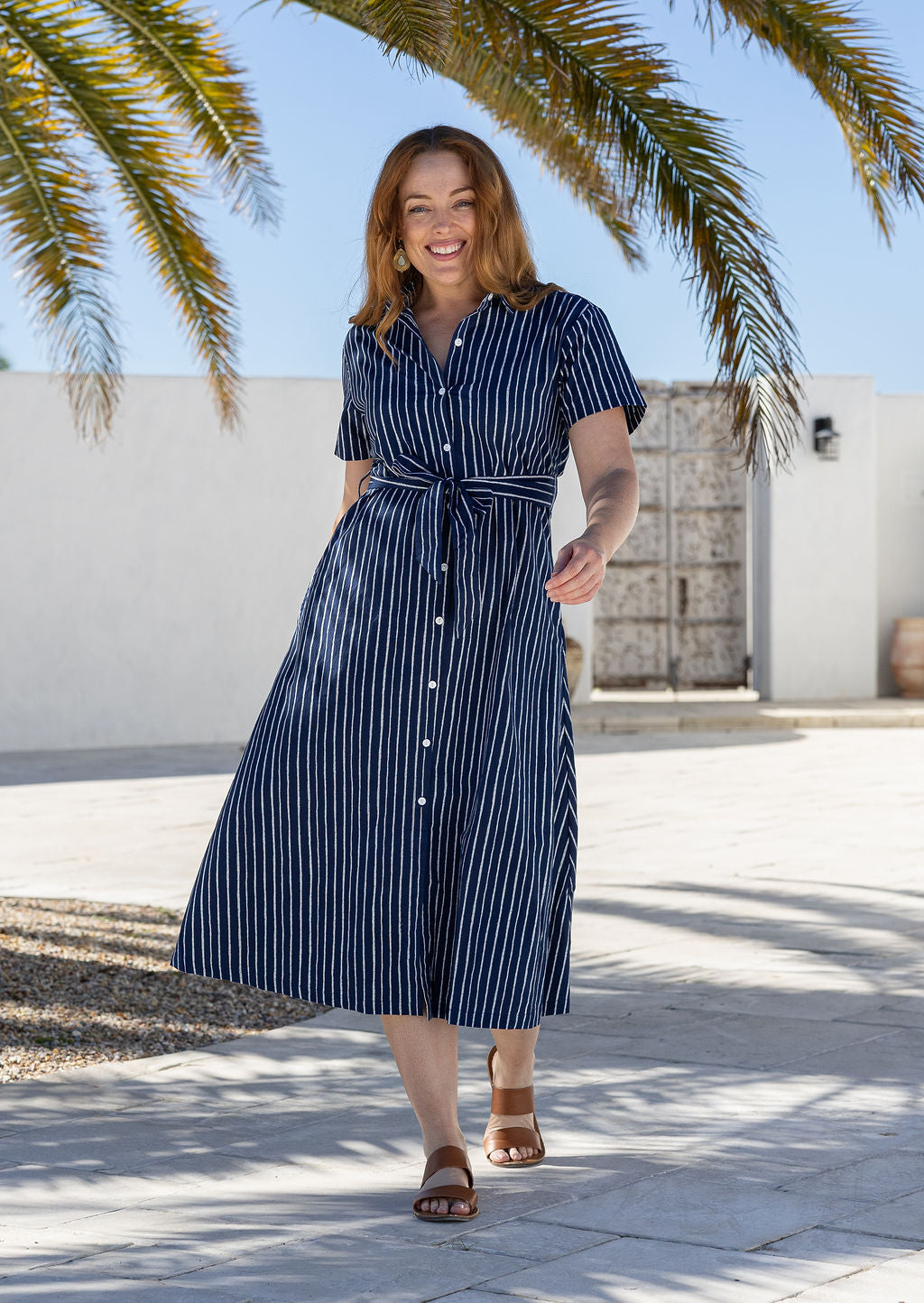 Model poses wears 1950s inspired, button through shirt style dress with collar, short sleeves, waist tie and pockets.