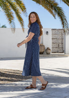 Woman stands sideways wearing cotton shirt dress with collar and T-shirt sleeves. 