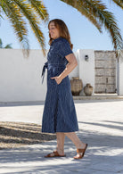 A woman wearing a navy blue based print midi dress with a tie waist and short sleeves, walking outdoors. 