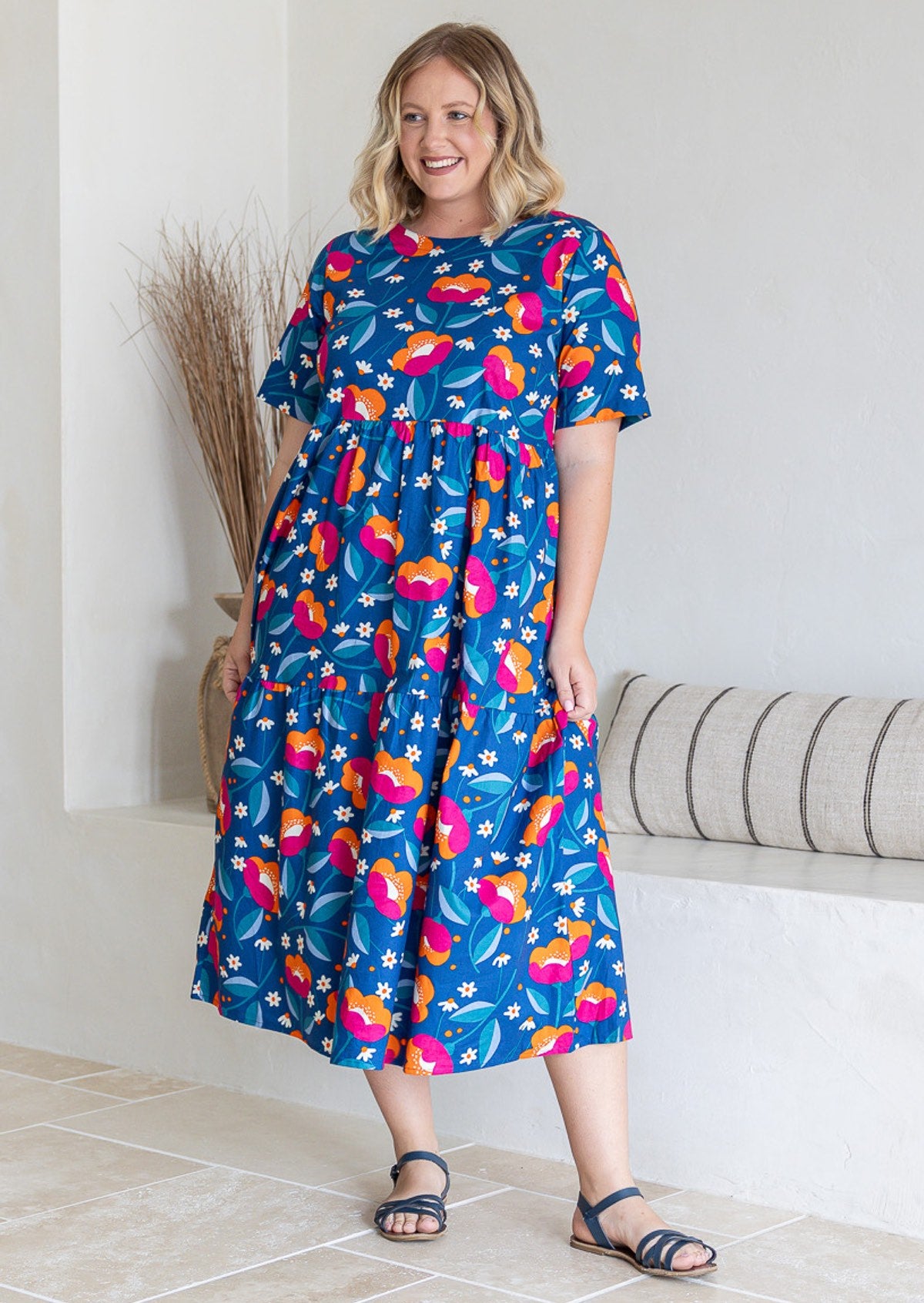 Woman posing in three tiered cotton midi length dress with short sleeves, in blue based graphic floral print