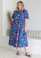 Woman posing in three tiered cotton midi length dress with short sleeves, in blue based graphic floral print