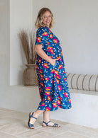 Model stands sideways wearing a floral print, relaxed fit cotton dress with tiers, and hand in pockets