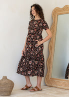 Woman wearing a relaxed fit printed black cotton dress with tiered design, standing next to a large mirror