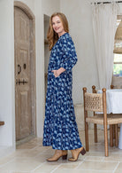 Woman stands side ways wearing a 100% cotton tiered maxi dress in navy based floral print with 3/4 sleeves, pockets and mandarin collar