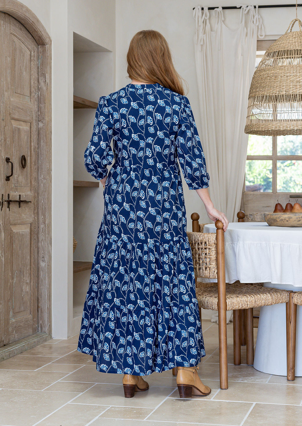 Woman standing backwards wearing a 100% cotton tiered maxi dress in floral print with 3/4 sleeves, pockets and mandarin collar