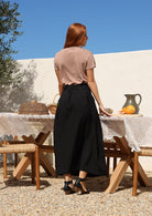 Woman stands backwards wearing a 100% cotton skirt in black with belt loops paired with plain basic top