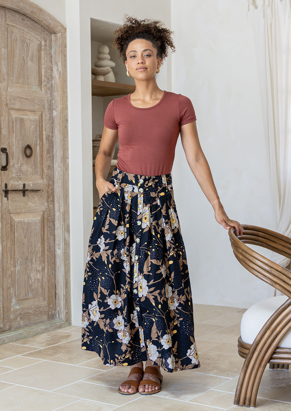 Woman wearing a pink basic rayon top and floral button through shin length cotton skirt with box pleats, belt loops and pockets.